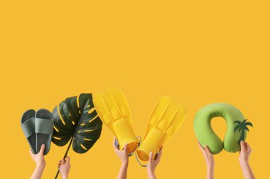 Plaj aksesuarları ve sarı arka planda palmiye yaprağı olan kadın elleri.