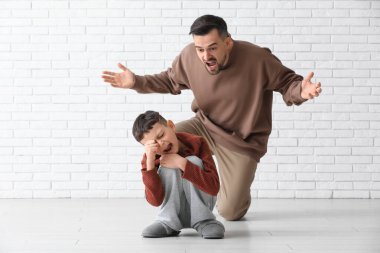 Kızgın baba ağlayan oğluna beyaz tuğla duvarın yanında bağırıyor.