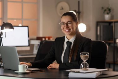 Bilgisayarla çalışan genç iş kadını akşamları masada oturuyor.