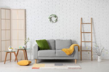 Gri kanepeli ve kahve masasına yumurta boyanmış şenlikli oturma odasının içi. Paskalya kutlaması