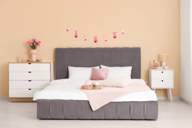 Konforlu yatağı, çelengi ve şifoniyerinde lale çiçekleri olan şenlikli bir yatak odası. Paskalya kutlaması