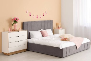 Konforlu yatağı, çelengi ve şifoniyerinde lale çiçekleri olan şenlikli bir yatak odası. Paskalya kutlaması