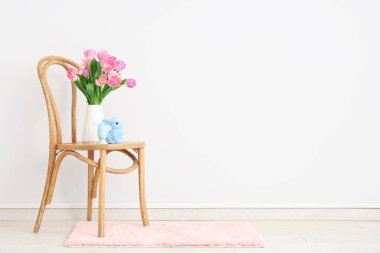 Vazo dolusu lale çiçeği, tavşan ve beyaz duvarın yanındaki sandalyeye boyanmış yumurta. Paskalya kutlaması