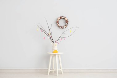 Süslü ağaç dalları olan vazo ve beyaz duvarın yanındaki taburede oturan piliçler. Paskalya kutlaması