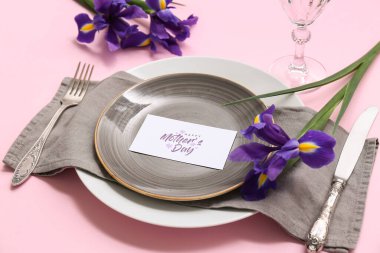 Tebrik kartı ve pembe arka planda süsen çiçekleri olan güzel bir masa, yakın plan. Anneler Günü kutlaması