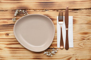 Çatal bıçaklı tabak, kağıt peçete ve ahşap arka planda çingene çiçeği.