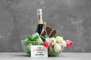 Anneler Günü için şampanya şişesi, lale ve çikolata dolu sepet gri grunge arka planda.