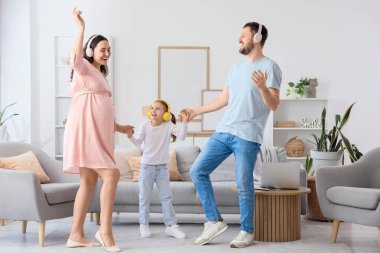 Babası ve kulaklıklı hamile annesiyle evde dans eden küçük mutlu bir kız.