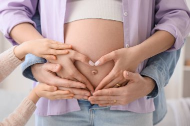 Evde babasıyla birlikte küçük bir kız hamile annenin karnına dokunuyor.