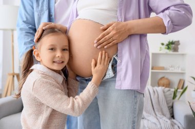 Sevimli küçük kız hamile annesinin karnına sarılıyor ve babası evde.