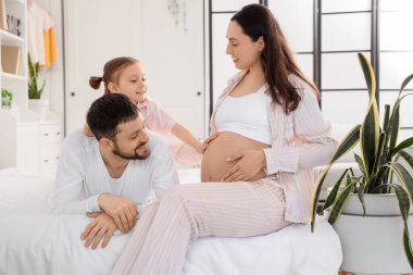 Sevimli küçük kız yatak odasında hamile annesinin karnına ve babasına dokunuyor.