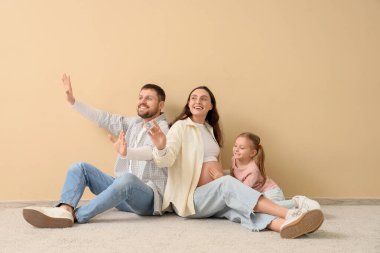 Bej duvarın yanında oturan hamile annesi ve babasıyla çok tatlı küçük bir kız.