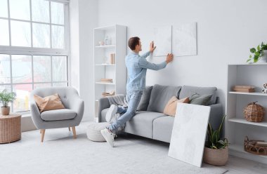 Evdeki ışık duvarına resim asan genç adam.