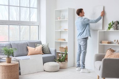 Genç adam oturma odasındaki ışık duvarına resim asıyor.