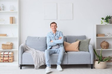 Oturma odasındaki tabloların yanında oturan genç adam.