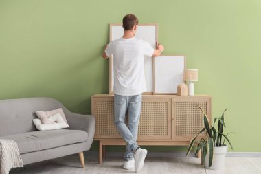 Evdeki çekmecelerin arkasında boş çerçeveleri olan genç bir adam.