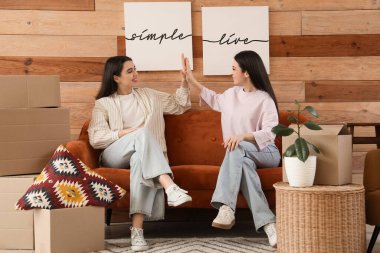 Evdeki kanepede birbirlerine beşlik çakan genç kadınlar posterleri asıyorlar.