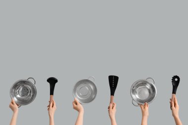 Gri arka planda colanders ve spatulaları olan kadın elleri