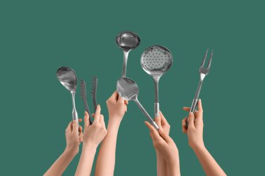 Yeşil arka planda gümüş mutfak aletleri olan kadın elleri.