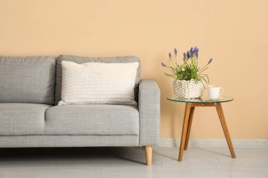 Güzel Muscari çiçekli bir masa, bir fincan kahve ve renkli duvarın yanında şık bir kanepe.