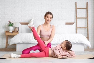 Sportif genç anne ve tatlı küçük kızı evde birlikte egzersiz yapıyorlar. Anneler Günü kutlaması