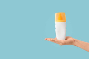 Mavi arka planda güneş kremi şişesi olan bir kadın el.