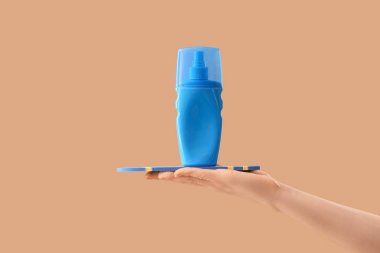 Elinde bej arka planda bir şişe güneş kremi olan mini sörf tahtası tutan bir kadın.