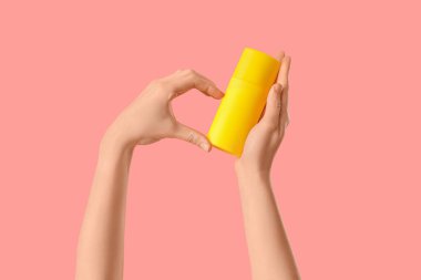 Kadın pembe arka planda güneş kremi şişesiyle kalp hareketi yapıyor.