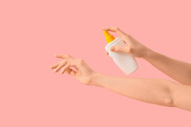 Kadın pembe arka plana güneş kremi sürüyor.
