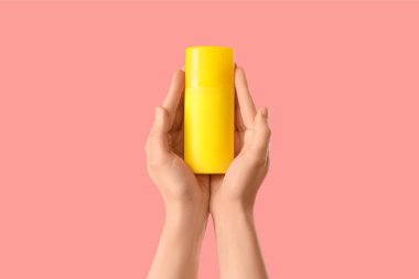 Pembe arka planda güneş kremi şişesi tutan kadın.