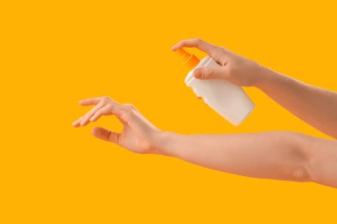 Sarı arka plana güneş kremi süren bir kadın.