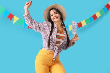 Hasır şapkalı, tebrik kartı ve mavi arka planda bayrakları olan genç ve mutlu bir kadın. Junina festivali.