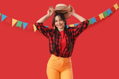Genç mutlu kadın kırmızı arka planda hasır şapkasını çıkarıyor. Junina festivali.