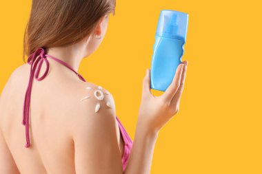 Omzunda güneş kreminden yapılmış bir kadın, sarı arka planda.