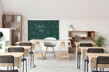 Sınıfın içinde karatahta, raf üniteleri ve masalar var. Okul yılı sonu.