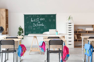 Sınıfın içinde karatahta, raf üniteleri ve masalar var. Okul yılı sonu.