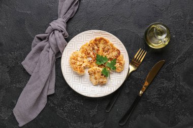 Siyah arka planda ızgara karnabahar bifteği ve maydanozlu tabak.