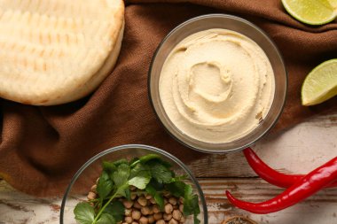 Bir kase lezzetli humus, malzemeler, ekmek ve peçeteyle birlikte ahşap arka planda.