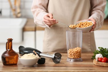 Genç kadın mutfaktaki masada humus için blender 'a nohut ekliyor.