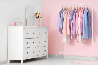 Farklı kadın kıyafetleri, aksesuarlar, çiçekler ve pembe duvarın yanındaki çekmecelerin üstündeki posterlerle doldur.