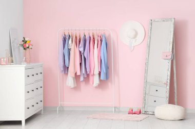 Farklı kadın kıyafetleri, ayna ve bahar çiçekleriyle modern soyunma odasının şık bir iç mekanı.