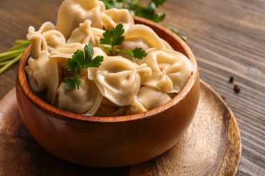 Tahta arka planda lezzetli kaynamış hamur köfteleri ve maydanozlu kase, yakın plan.