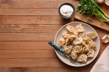 Maydanozlu kaynamış hamur köftesi ve ahşap zemin üzerinde bir kase ekşi krema.