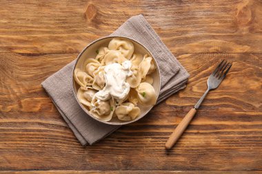 Bir kase lezzetli kaynamış köfte, ekşi krema ve ahşap zemin üzerinde yeşil soğan.