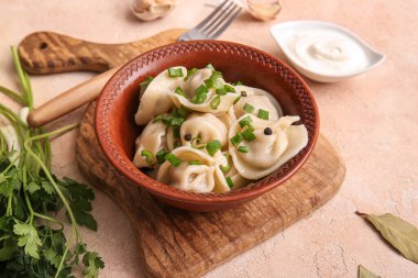 Bir kase lezzetli haşlanmış hamur köftesi, yeşil soğan ve bej arka planda ekşi krema, yakın plan.