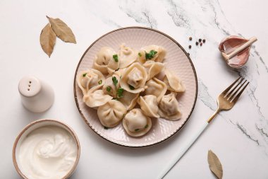 Maydanozlu kaynamış hamur köftesi ve beyaz arka planda bir kase ekşi krema.