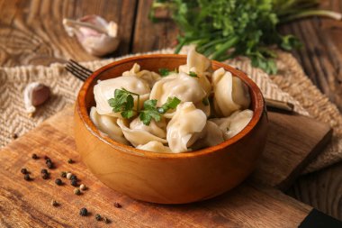 Tahta arka planda maydanozlu ve sarımsaklı bir kase lezzetli haşlanmış hamur köftesi.