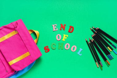 Okulun renkli harflerden, farklı kalemlerden ve yeşil arkaplandaki şık sırt çantasından oluşan metin sonu