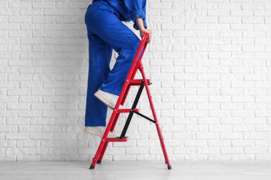 Beyaz tuğla duvarın yanındaki merdivenlere tırmanan kadın işçiler.