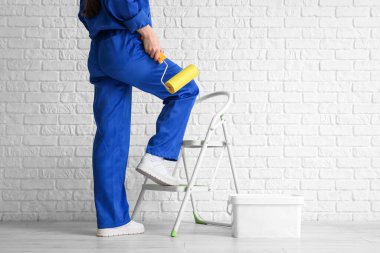 Beyaz tuğla duvarın yanında merdiven ve boya silindirli kadın işçi.